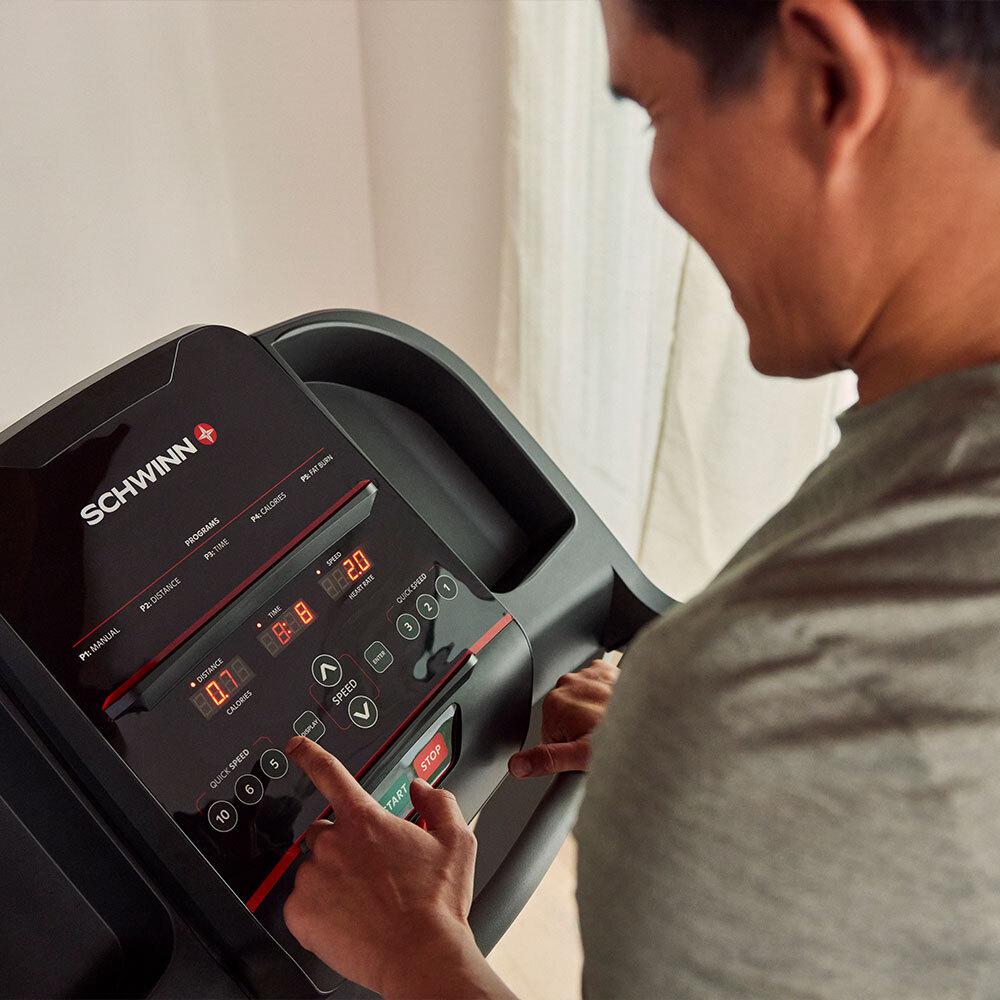 A man uses a Schwinn treadmill, touching the display screen. The screen shows speed, time, distance, and calories.