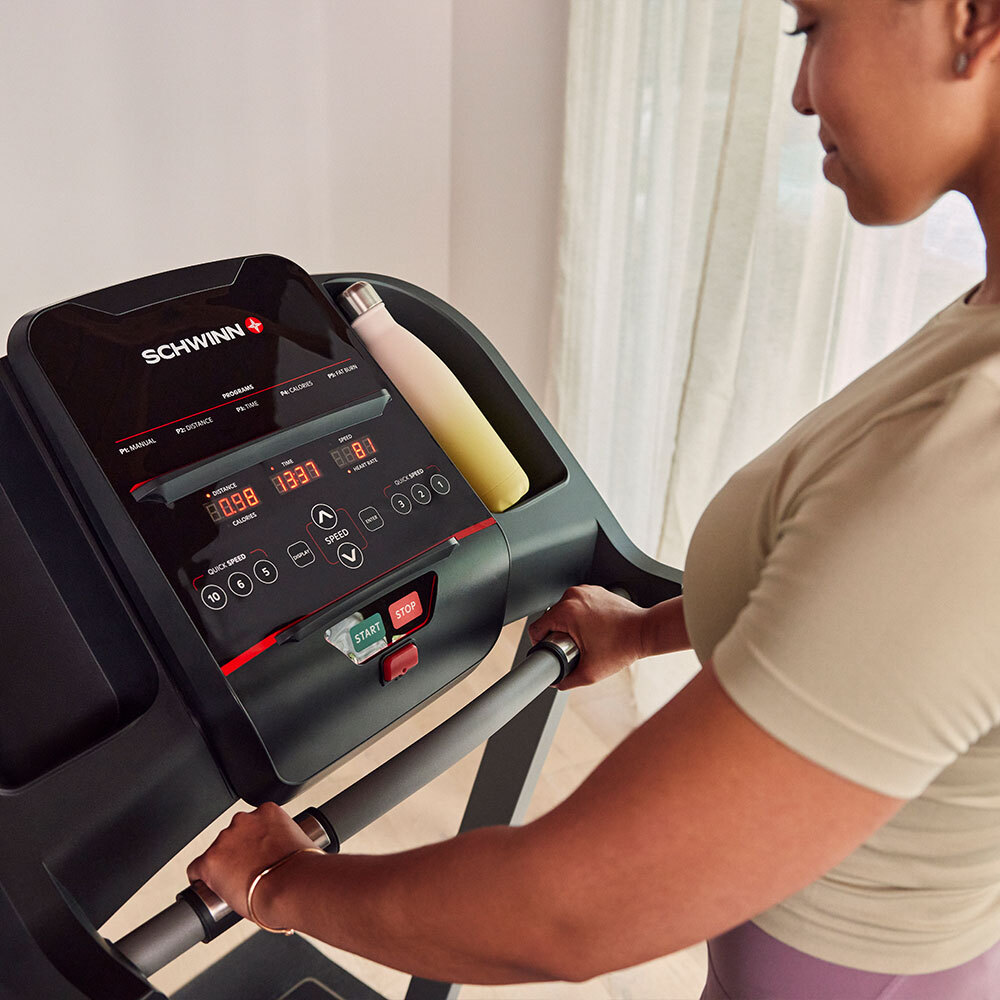 Woman on treadmill, holding handles. Treadmill displays distance, time, and speed. Water bottle rests in a holder. 