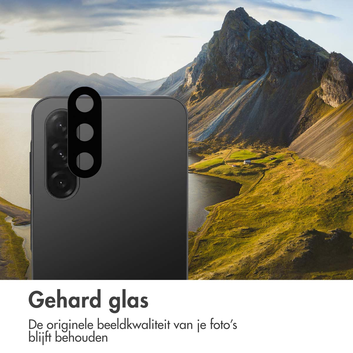 Een telefoon met lensbeschermer staat voor een berglandschap met een meer en groene velden. De lucht is bewolkt.