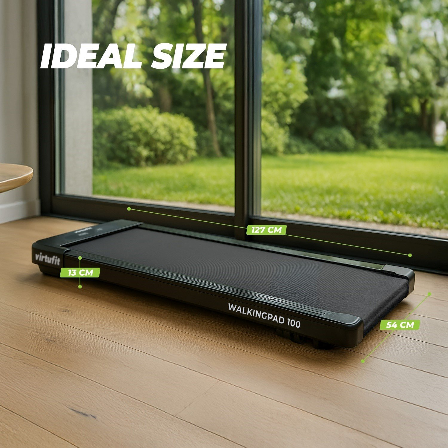 Un walkingpad 100 nero su pavimento in legno, dimensioni: 127 cm lungo, 54 cm largo, 13 cm alto. Lo sfondo mostra un giardino verde.