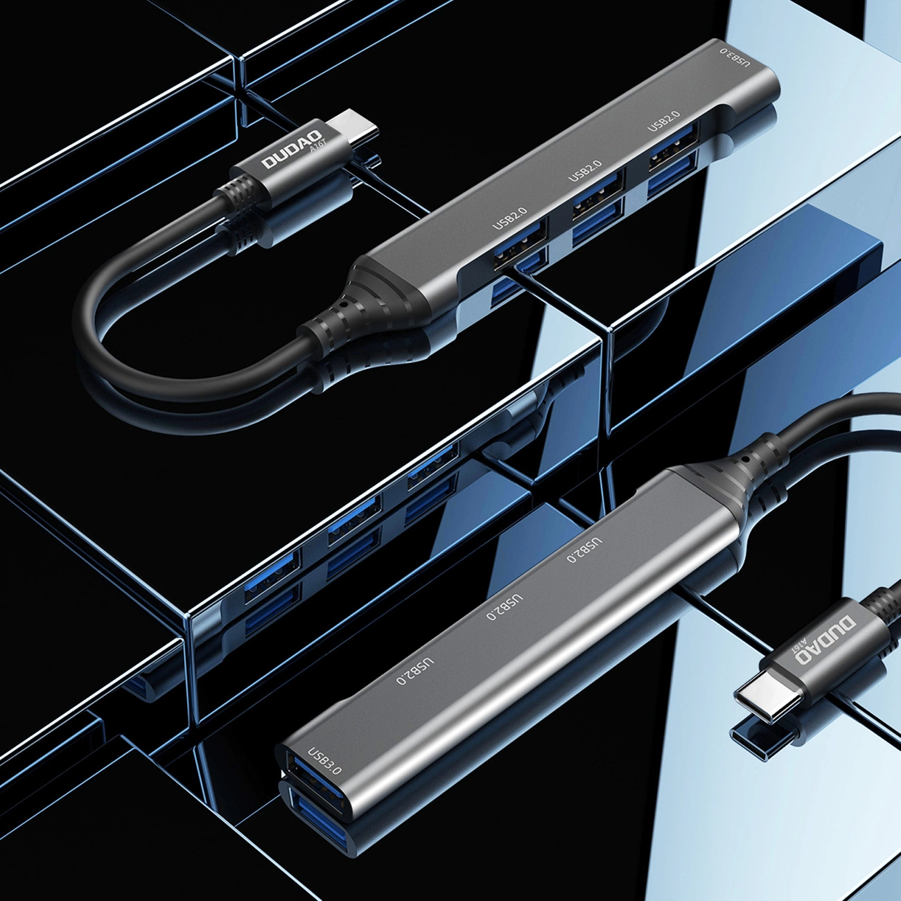 Due hub USB grigi su una superficie riflettente. Ogni hub ha più porte USB e un cavo USB-C collegato. Sfondo blu riflettente.