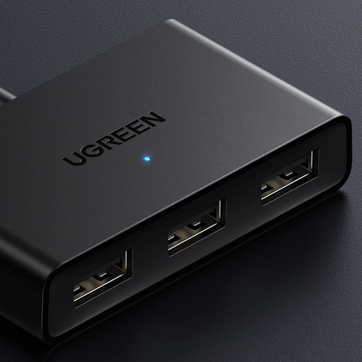 Un primo piano di un hub USB UGREEN nero con tre porte. Ha il marchio in alto e una luce blu.