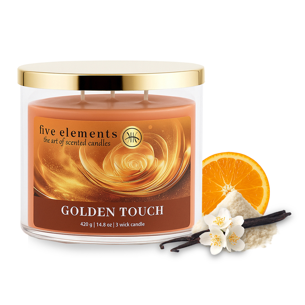 Duftkerze mit Golddeckel, orangefarbenem Wachs und 'Golden Touch'-Etikett. Daneben Orangenscheibe, Vanilleschoten, weiße Blumen und Pulver.