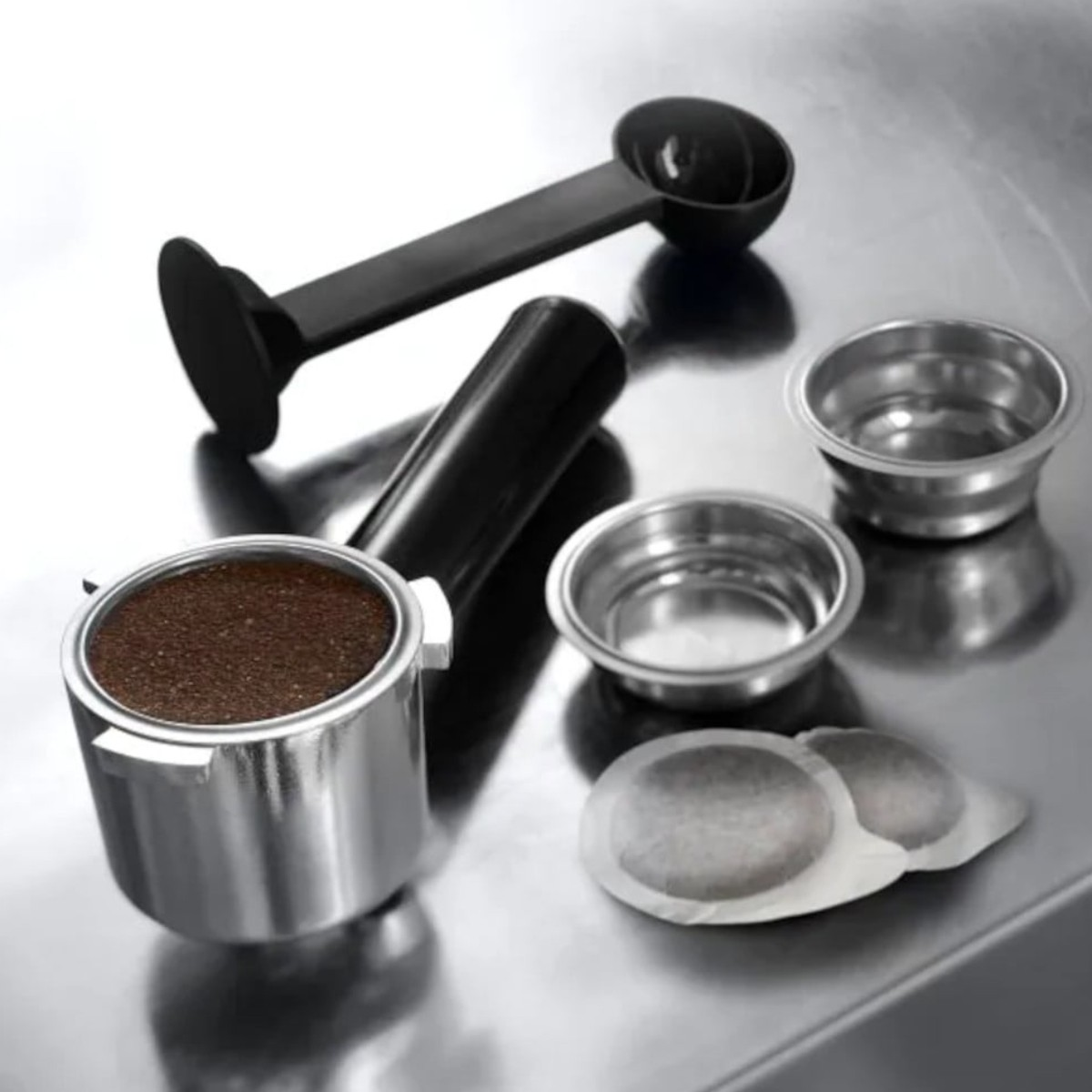 Części ekspresu do kawy: kolba z kawą mieloną, dwa koszyki filtrujące, saszetki kawy, miarka i uchwyt.