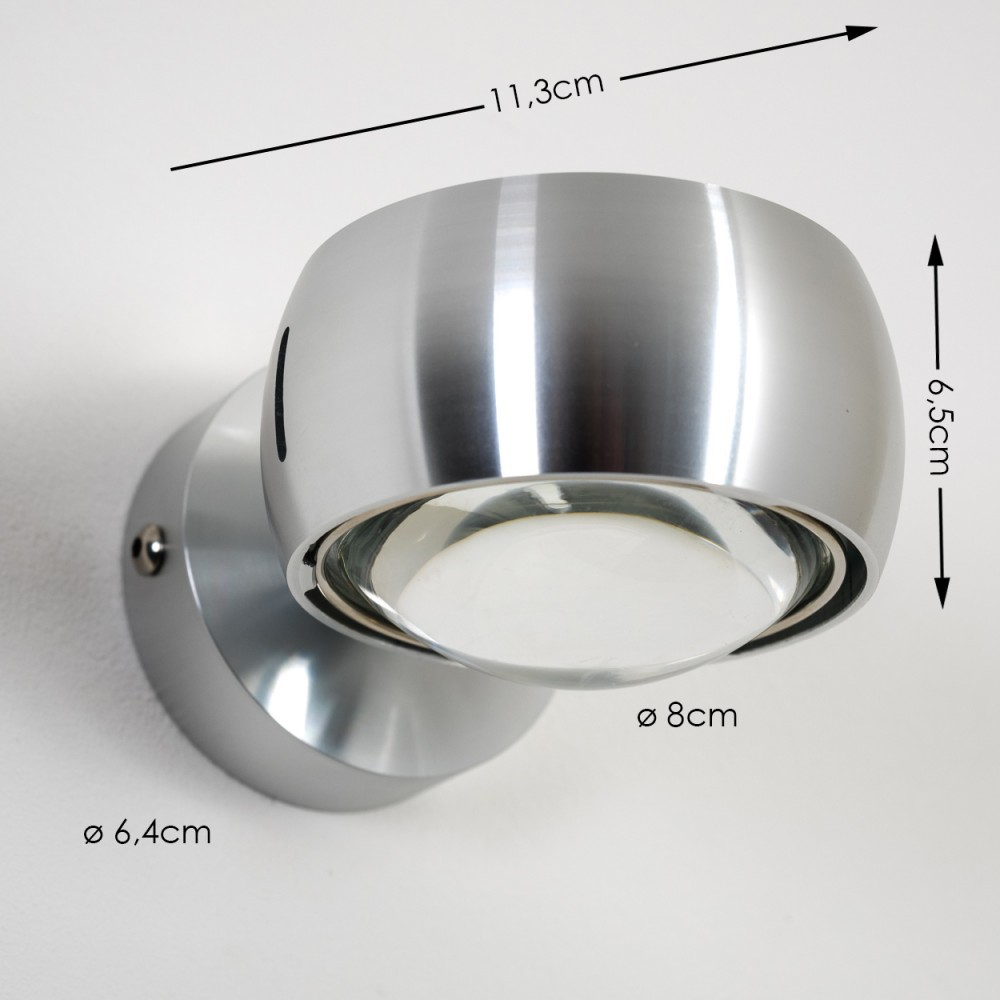 Eine metallische, kugelförmige Wandleuchte mit Maßangaben. Die Lampe ist silberfarben und an einer weißen Wand montiert. Klare Glaslinse.