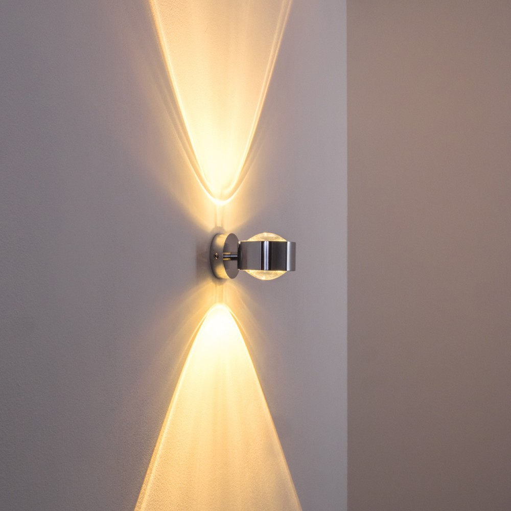 Eine moderne Wandleuchte ist an einer hellgrauen Wand angebracht. Sie strahlt Licht nach oben und unten aus.
