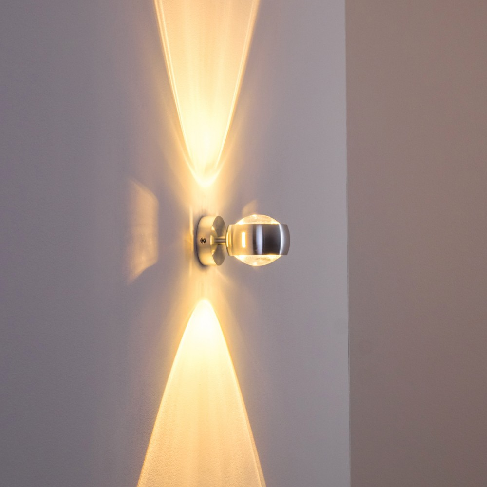 Eine moderne Wandleuchte ist an einer hellgrauen Wand angebracht und strahlt Lichtstrahlen nach oben und unten aus.