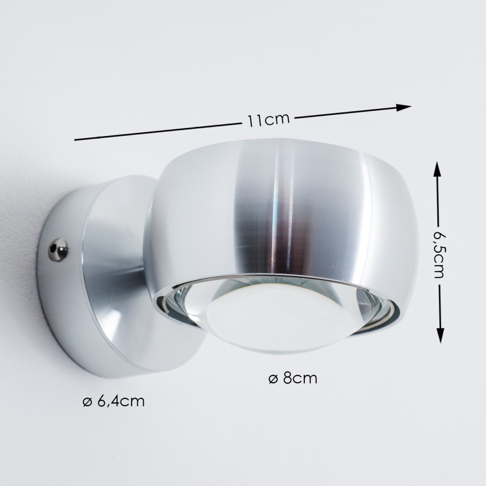 Eine metallische Wandleuchte ist an einer weißen Wand montiert. Abmessungen: 11cm, 6,5cm, 8cm und 6,4cm. Die Lampe hat eine Glühbirne.