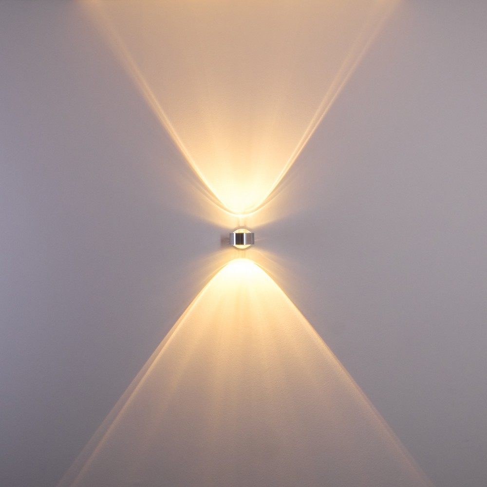 Eine Wandleuchte strahlt Licht nach oben und unten aus und erzeugt ein symmetrisches Muster. Die Wand ist hellgrau.
