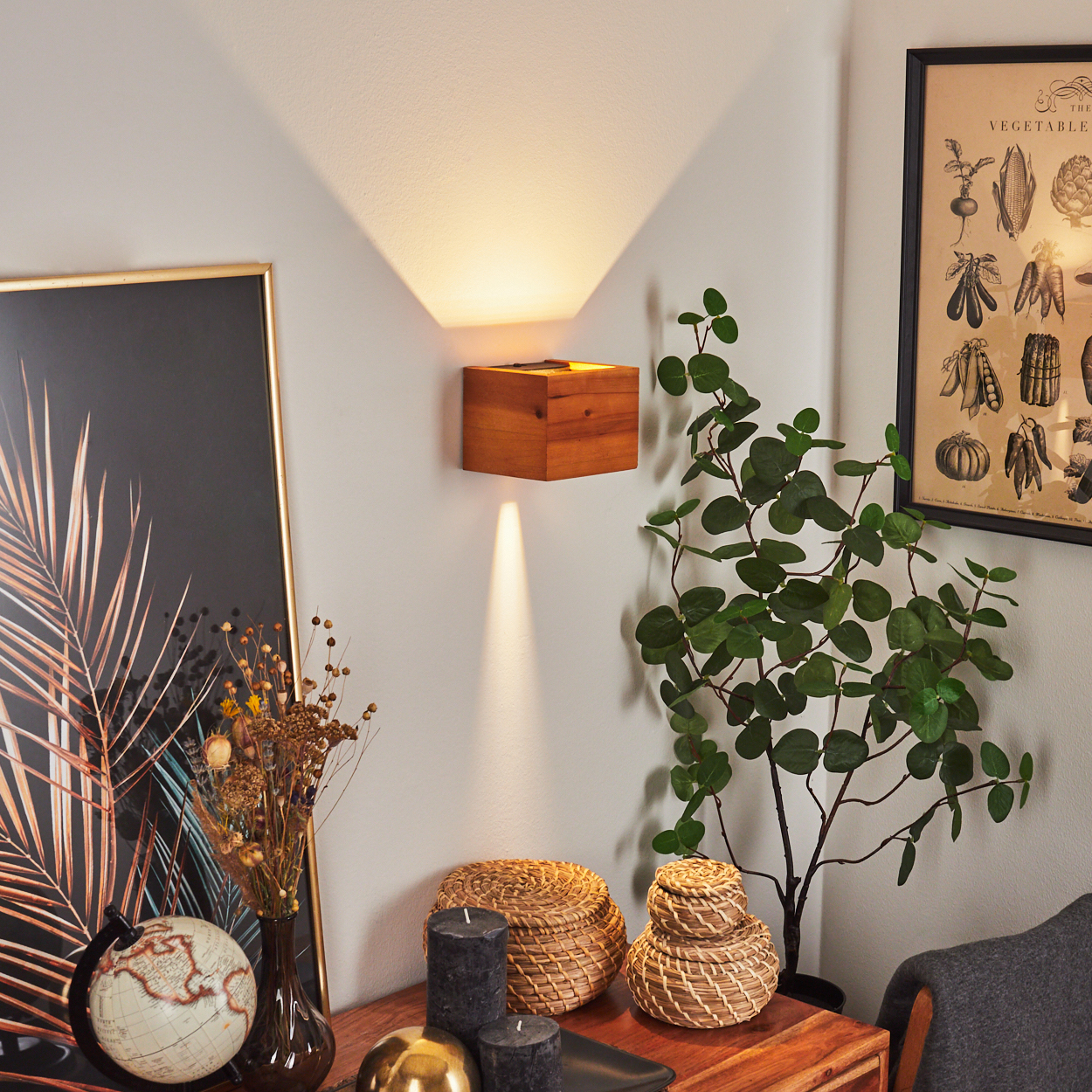 Holzwandlampe beleuchtet die Wand. Ein gerahmtes Poster, Pflanzen, Kerzen und Dekor stehen auf einem Holztisch.