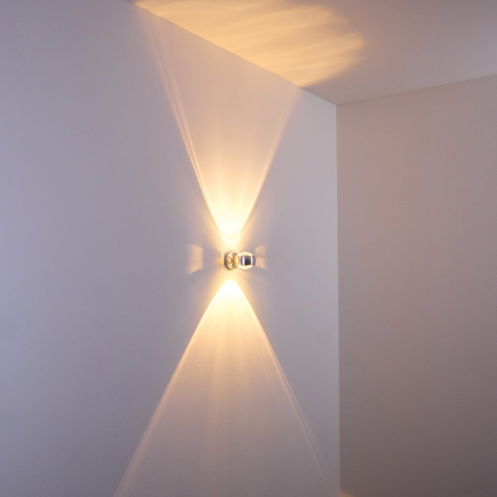 Eine moderne Wandleuchte an einer weißen Wand. Das Licht wirft zwei Strahlen in entgegengesetzte Richtungen und erzeugt einen visuellen Effekt.