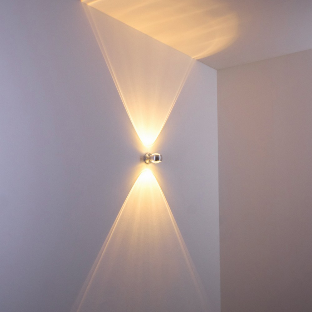 Eine moderne Wandleuchte strahlt Licht in zwei entgegengesetzte Richtungen aus und erzeugt ein symmetrisches Muster an der weißen Wand.