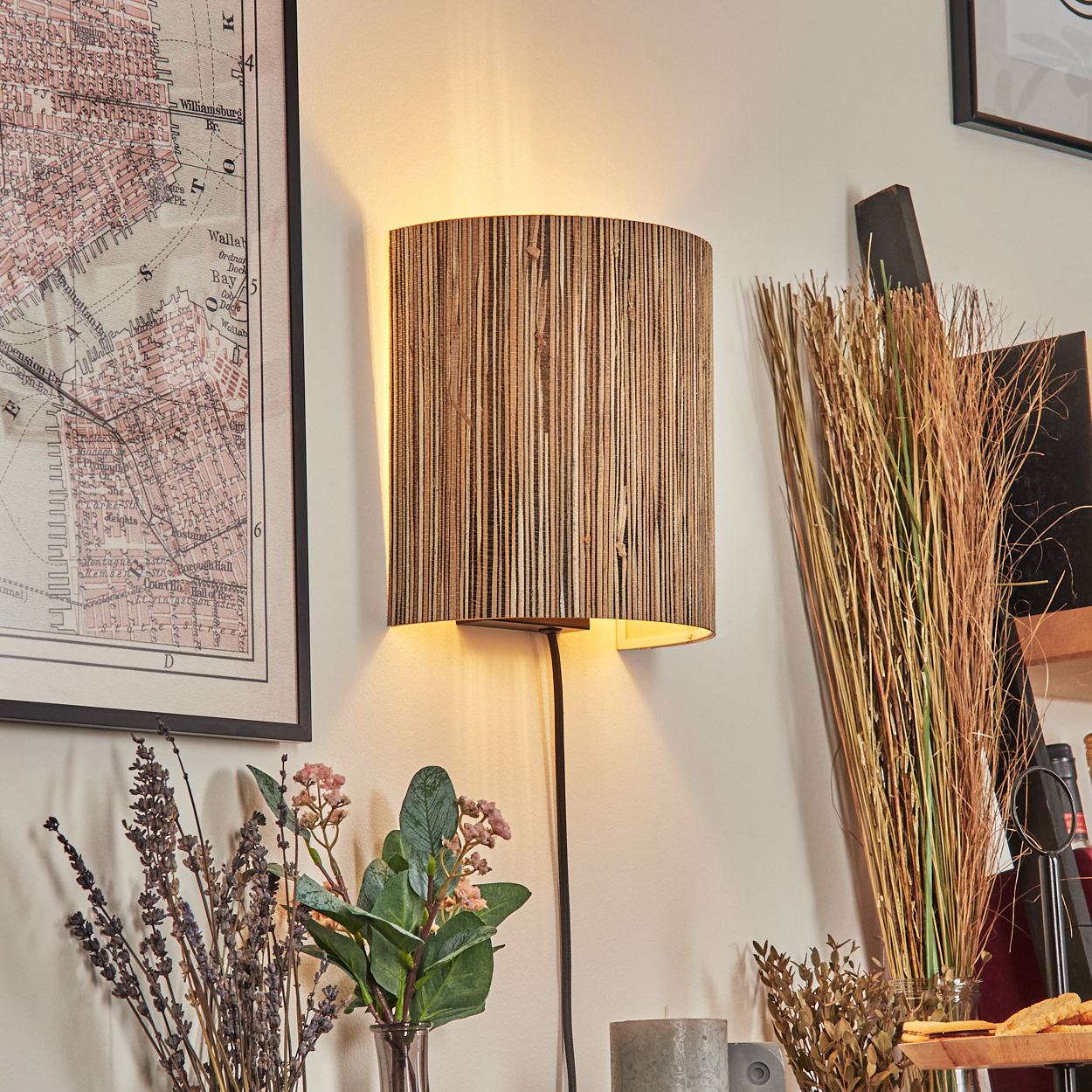 Eine Lampe mit Holzschirm an der Wand. Karte, Blumen und trockenes Gras sind ebenfalls zu sehen.