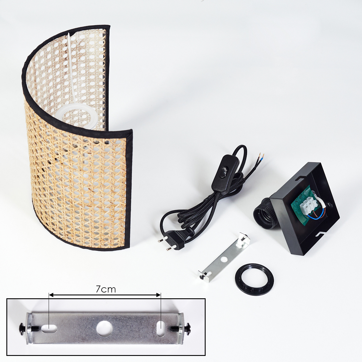 Eine zerlegte Wandlampe mit Rattanschatten, schwarzem Kabel, Schalter und Montagematerial auf weißer Oberfläche.