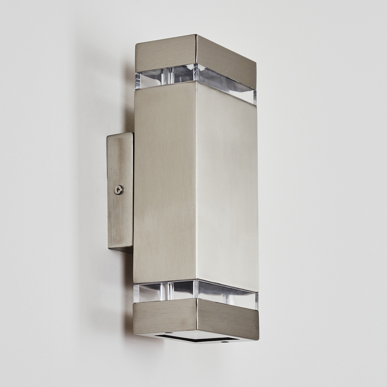 Eine moderne, rechteckige Wandleuchte mit gebürsteter Metalloberfläche, montiert an einer weißen Wand. Klare Paneele oben und unten.