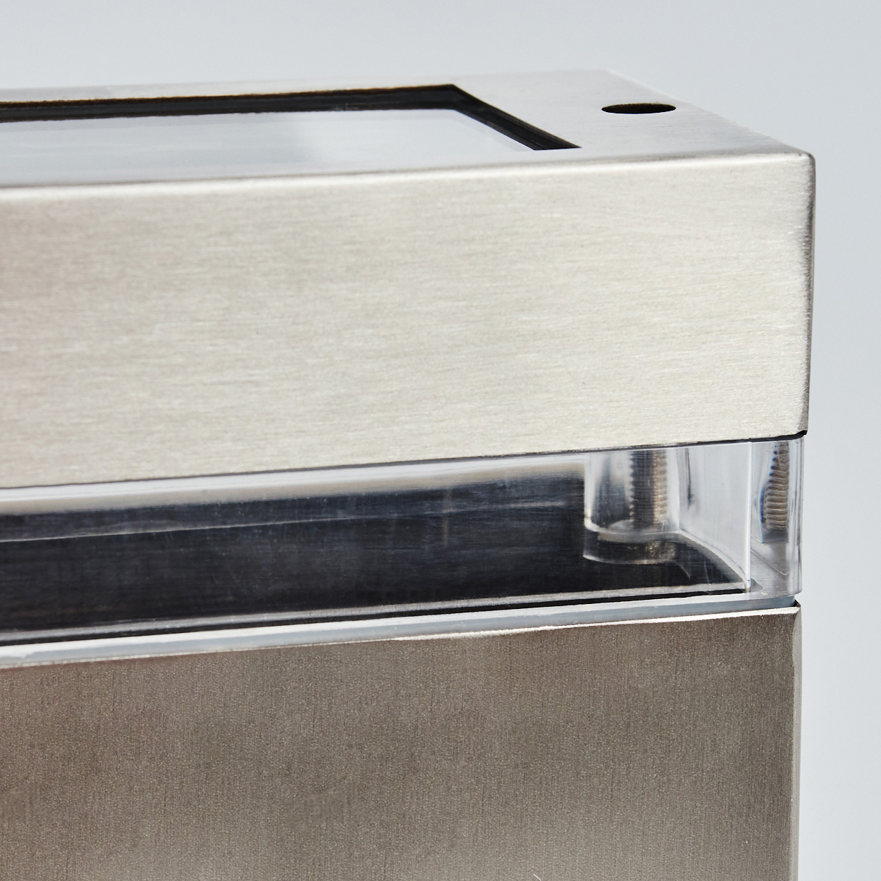 Nahaufnahme einer Metallbox mit transparentem Bereich. Die Box besteht aus gebürstetem Metall und klarem Kunststoff, auf weißem Hintergrund.