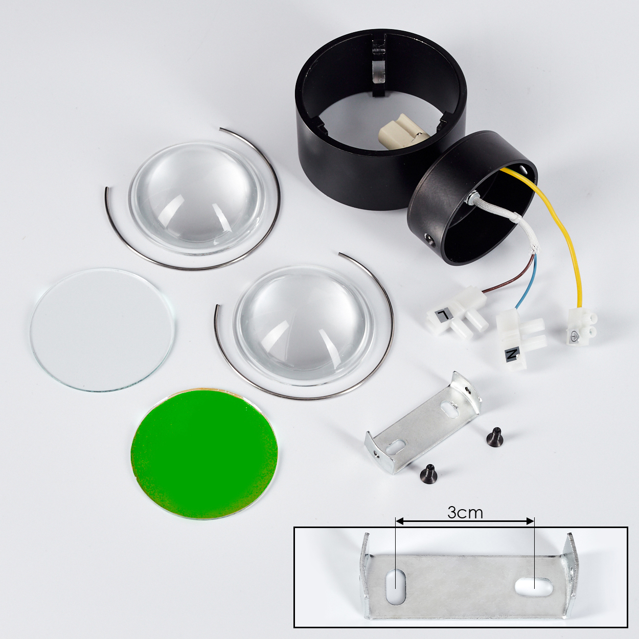 Komponenten für eine Lampe: Linsen, schwarze Zylinderteile, Verkabelung, eine Halterung und eine grüne Scheibe. Ein 3-cm-Lineal ist enthalten.