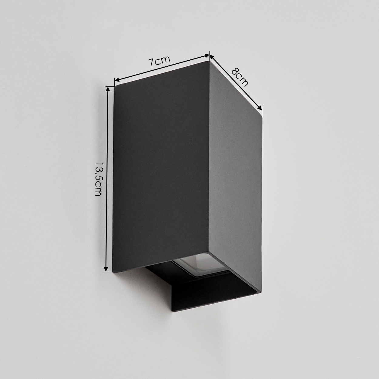 Eine schwarze, an der Wand montierte Leuchte mit angegebenen Abmessungen. Sie hat eine rechteckige Kastenform mit offenem Boden, an einer weißen Wand montiert.