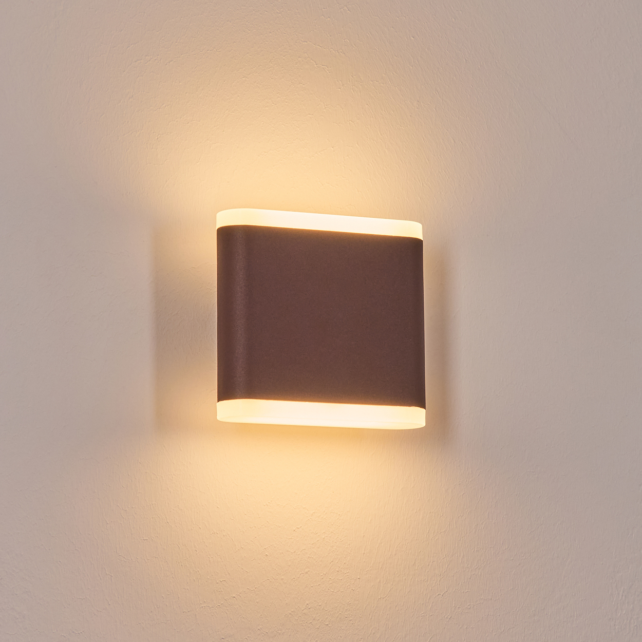 Eine moderne Wandlampe mit dunkelbrauner Front, die warmes Licht ausstrahlt. Sie ist an einer strukturierten, hellbeigen Wand angebracht.