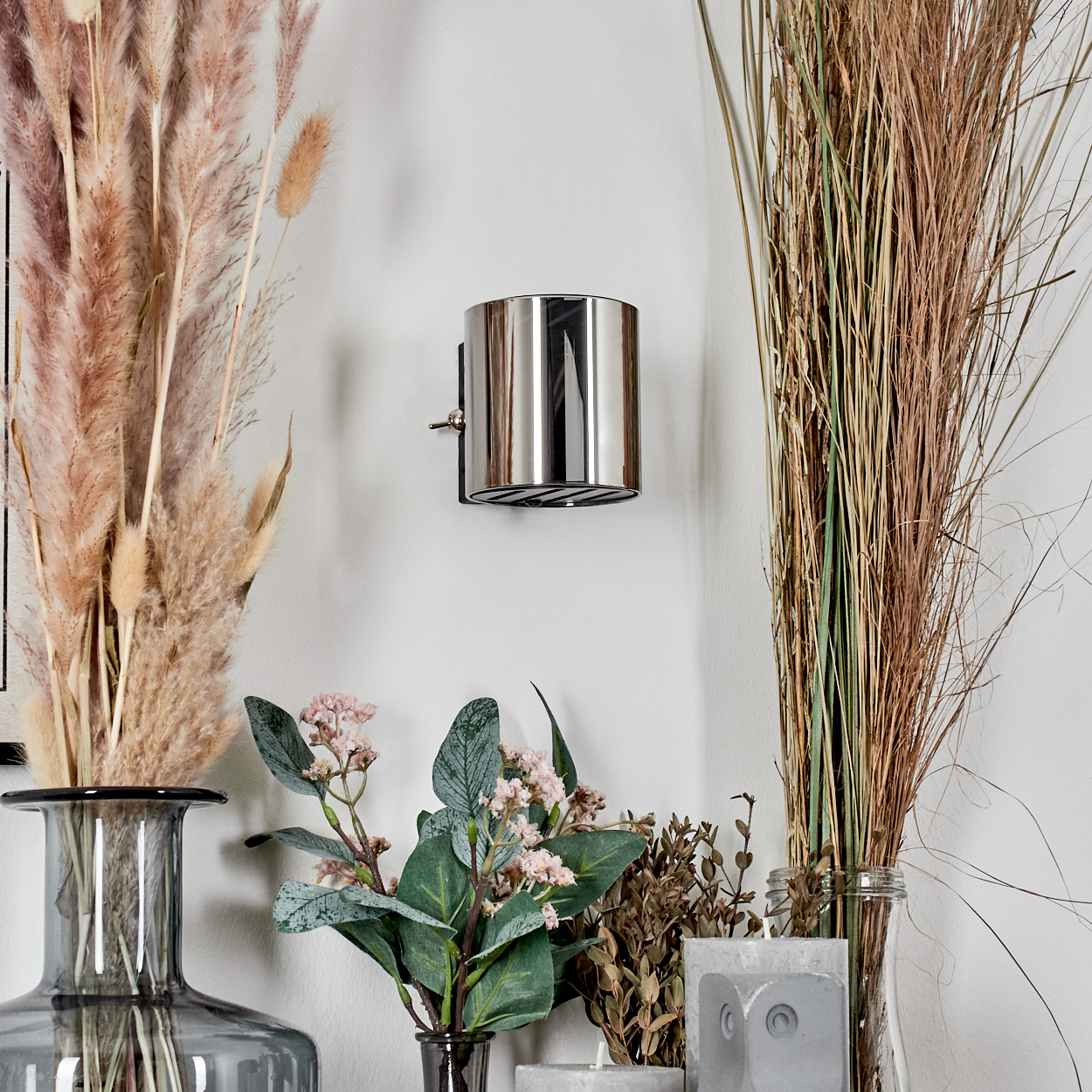 Silberne Wandlampe, Pampasgras, dekorative Pflanzen in Vasen an weißer Wand. Dekorative Einrichtung mit Blumen und Kerzen.