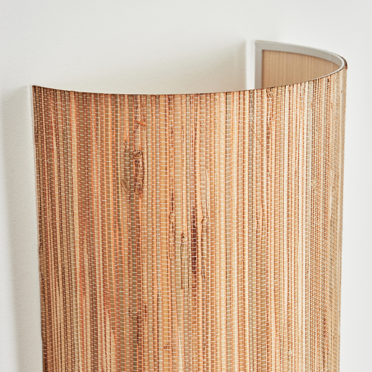 Nahaufnahme eines Lampenschirms aus Naturfasern, beige und braune Farbtöne, vor einer weißen Wand.