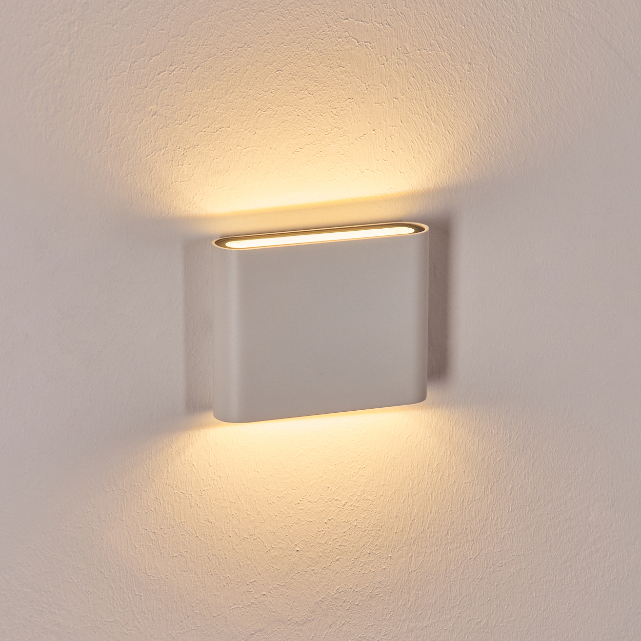 Eine moderne, rechteckige Wandleuchte strahlt warmes Licht auf eine strukturierte weiße Wand. Das Licht ist hellgrau.