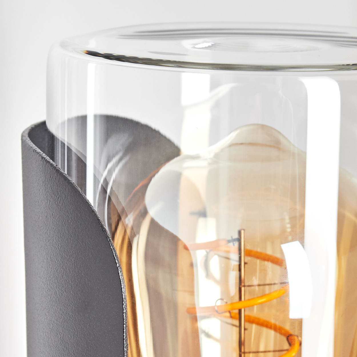 Nahaufnahme einer Glühbirne. Eine Glasabdeckung ist sichtbar, mit einem Metallrahmen. Die Glühbirne hat einen spiralförmigen orangefarbenen Glühfaden.