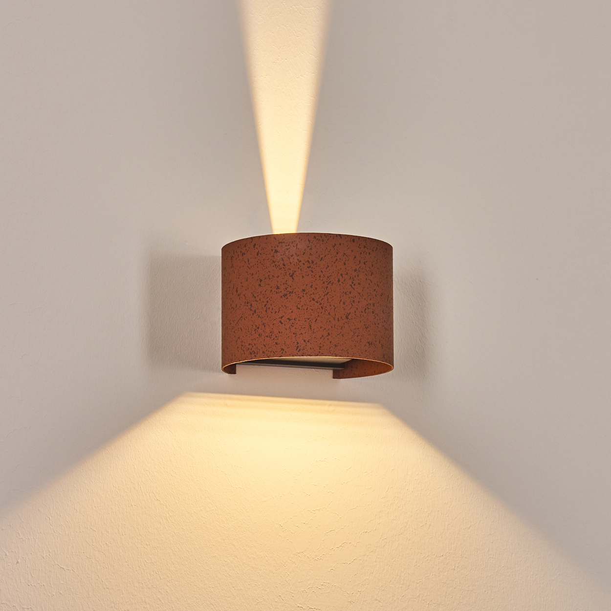 Eine rostbraune Wandlampe ist an einer weißen Wand befestigt und wirft Licht nach oben und unten.