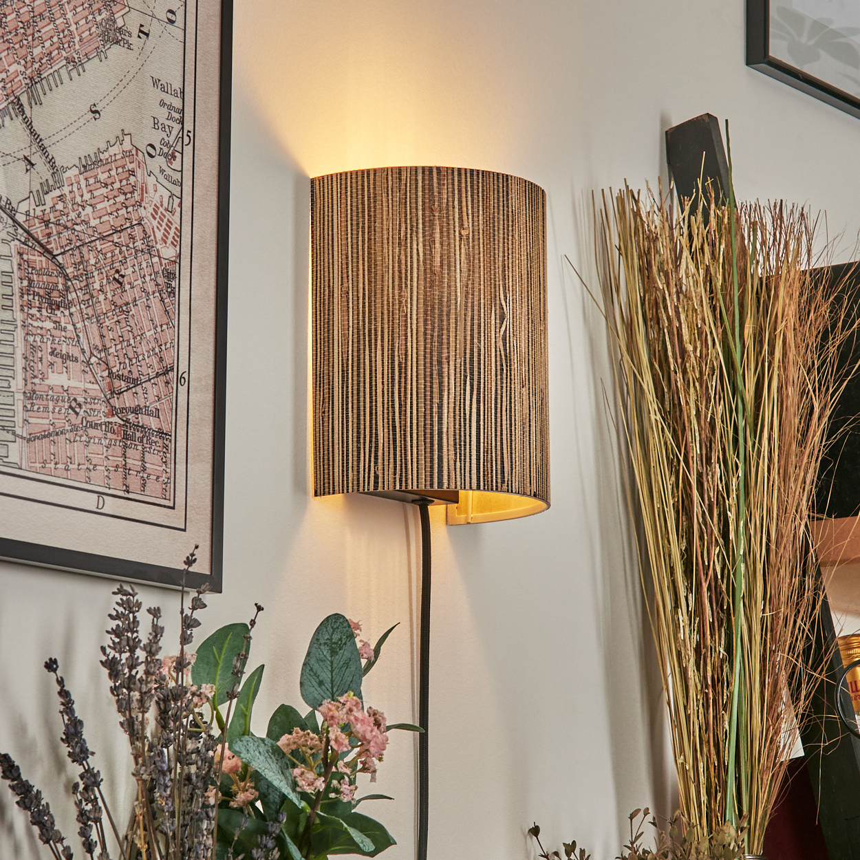 Eine Wandlampe mit strukturiertem Schirm ist beleuchtet. Eine Karte, Blumen und hohes Gras sind ebenfalls sichtbar.