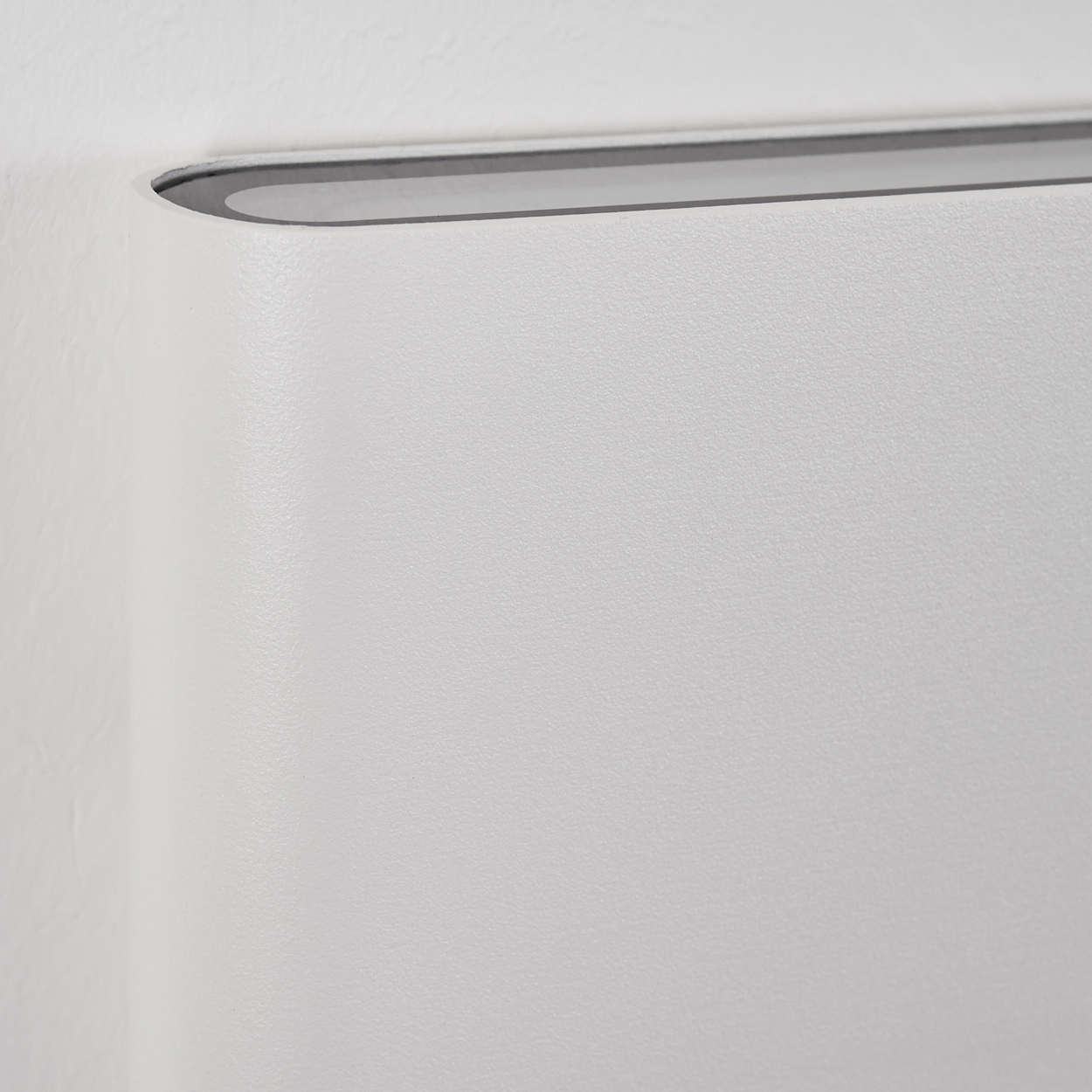 Nahaufnahme einer weißen Wand mit abgerundeter Kante. Ein dunkelgrauer Zierrat verläuft am Rand und bildet eine Kontrastlinie.