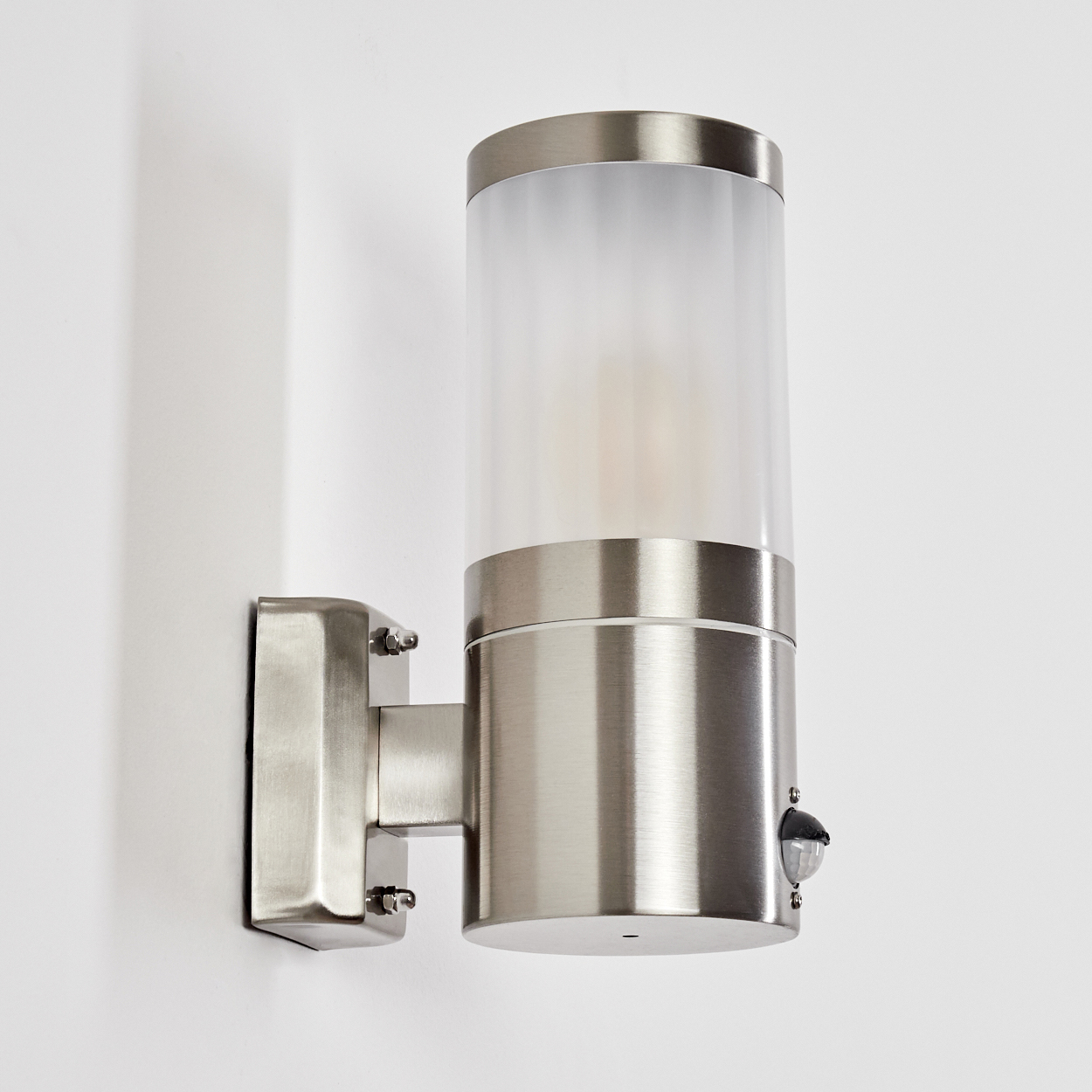 Eine metallische zylindrische Außenwandleuchte mit einem Zylinder aus Milchglas. Sie ist an einer weißen Wand montiert.
