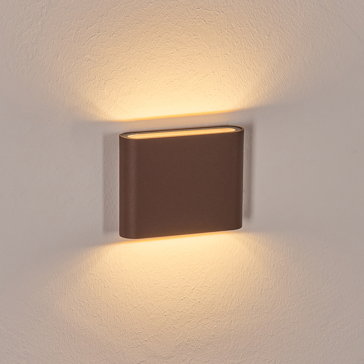 Eine braune, rechteckige Wandleuchte mit warmem Licht ist an einer strukturierten, cremefarbenen Wand montiert. Lichtstrahlen nach oben und unten.
