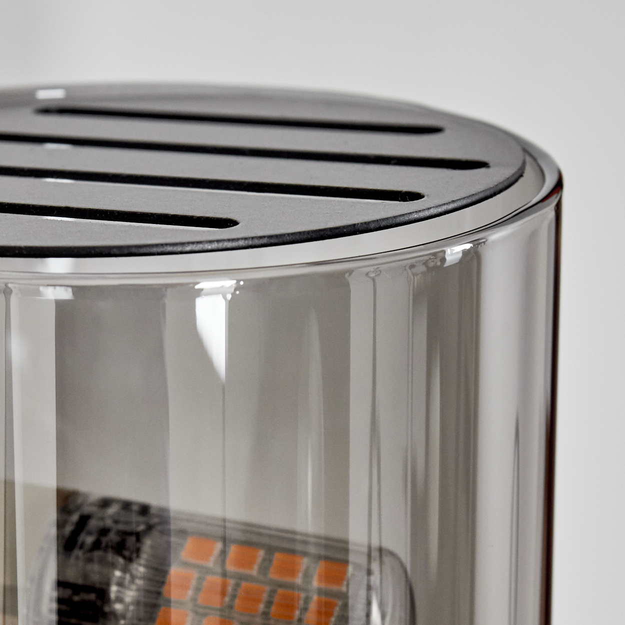 Nahaufnahme eines Glaszylinders mit geschlitztem Metalldeckel. Innen orangefarbene Quadrate. Weißer Hintergrund.