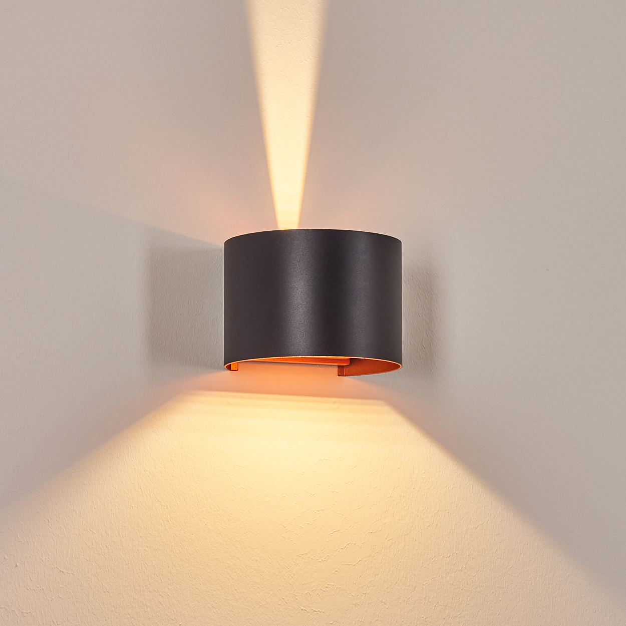 Eine moderne schwarze Wandleuchte mit orangefarbenem Innenraum, die Licht nach oben und unten an eine hellbeige Wand wirft.