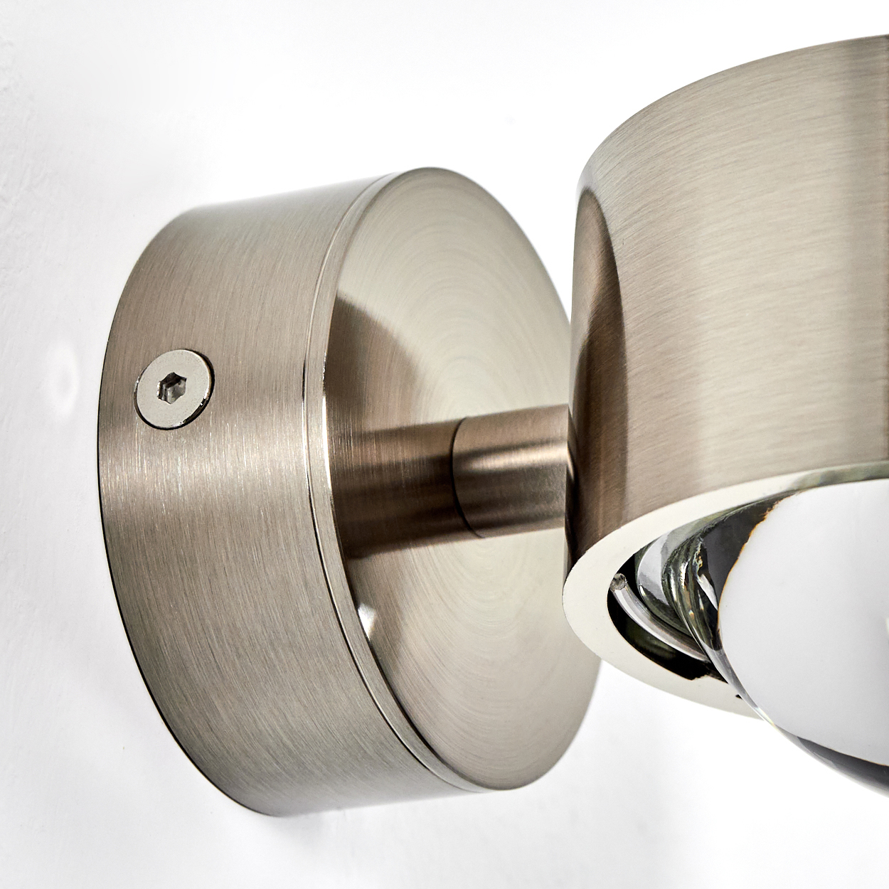 Nahaufnahme einer Wandlampe aus gebürstetem Metall. Die Lampe besteht aus zwei zylindrischen Teilen und einer Glühbirne.