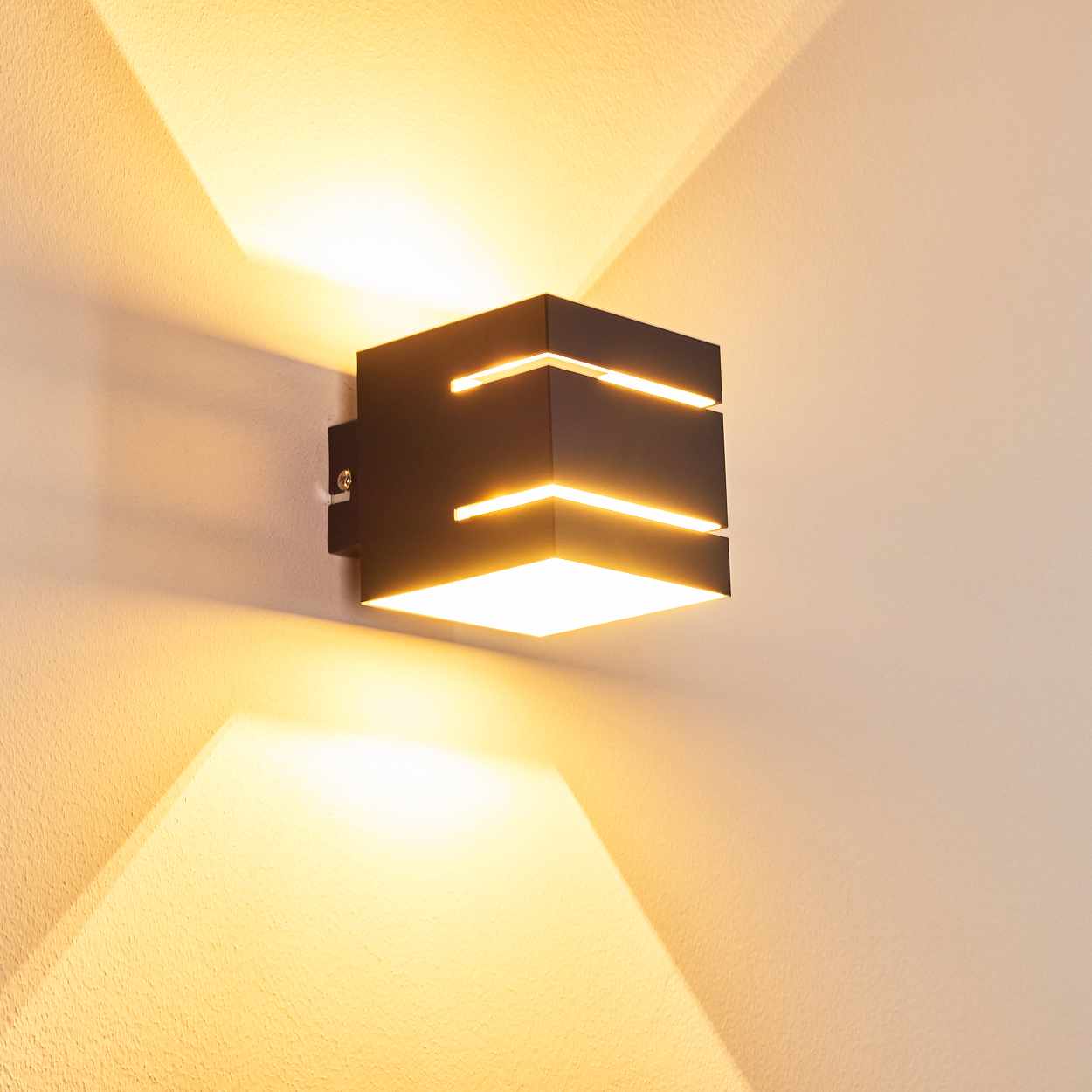 Eine moderne schwarze Wandleuchte mit hellem, warmem Licht. Sie wirft einen quadratischen Strahl nach unten und ein Dreieck nach oben auf die weiße Wand.