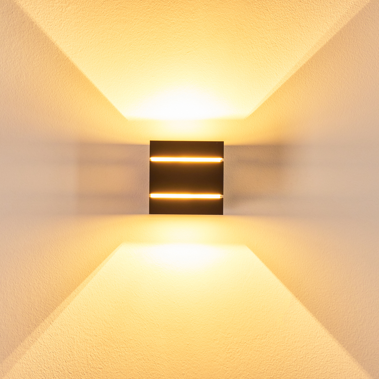 Eine moderne Wandleuchte mit drei horizontalen Lichtstreifen, die nach oben und unten Licht auf eine strukturierte weiße Wand wirft.