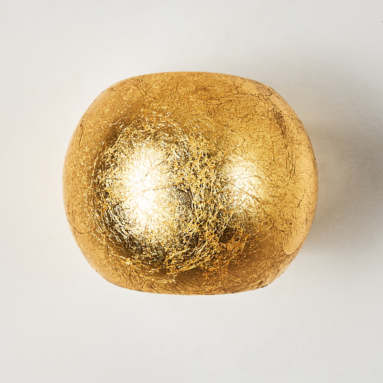 Eine goldene, strukturierte Kugel vor weißem Hintergrund. Die Oberfläche der Kugel scheint mit Blattgold bedeckt zu sein.