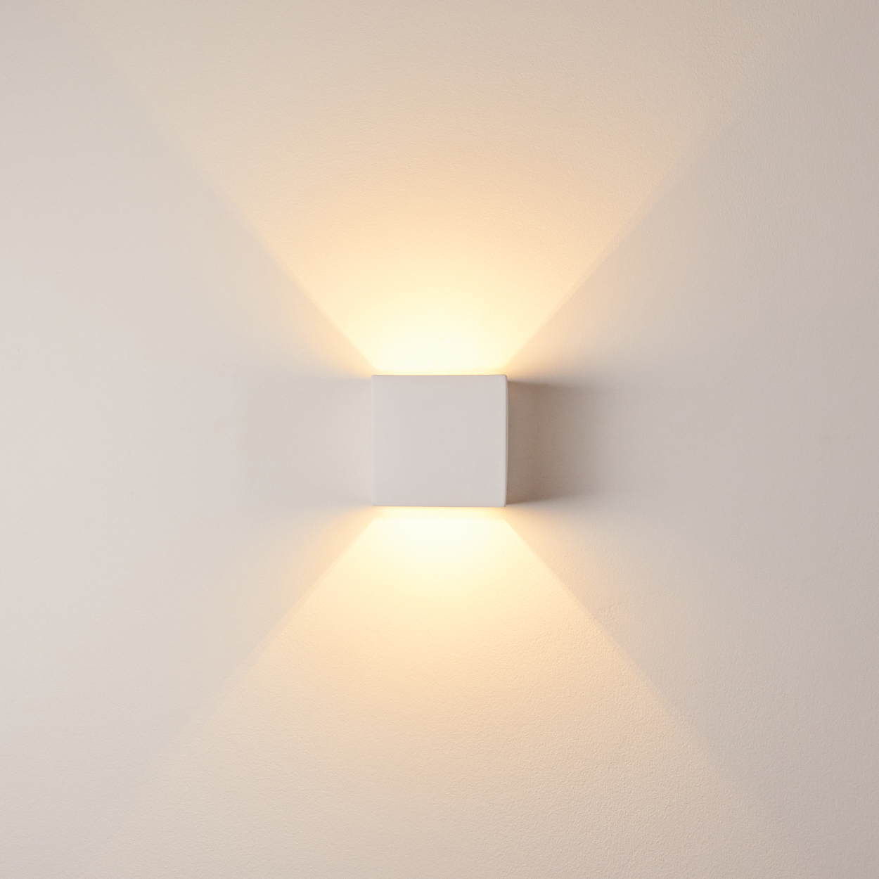 Eine quadratische weiße Wandleuchte strahlt Licht nach oben und unten auf eine hellbeige Wand.