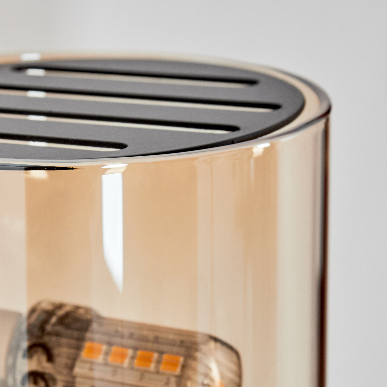 Nahaufnahme einer Glaslampe mit schwarzer Oberseite. Die Lampe hat eine hellbraune Tönung. Ein Teil der Glühbirne ist sichtbar.