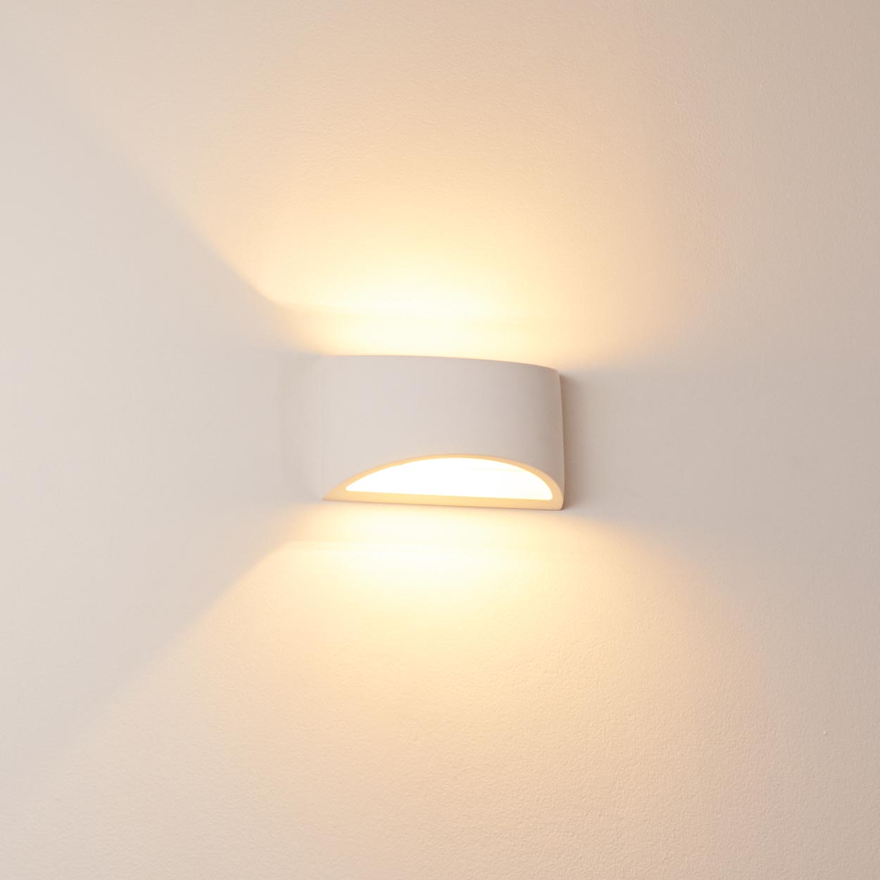 Eine weiße Wandleuchte strahlt warmes Licht aus. Die Lampe hat eine gebogene Form und wirft Licht nach unten und oben.