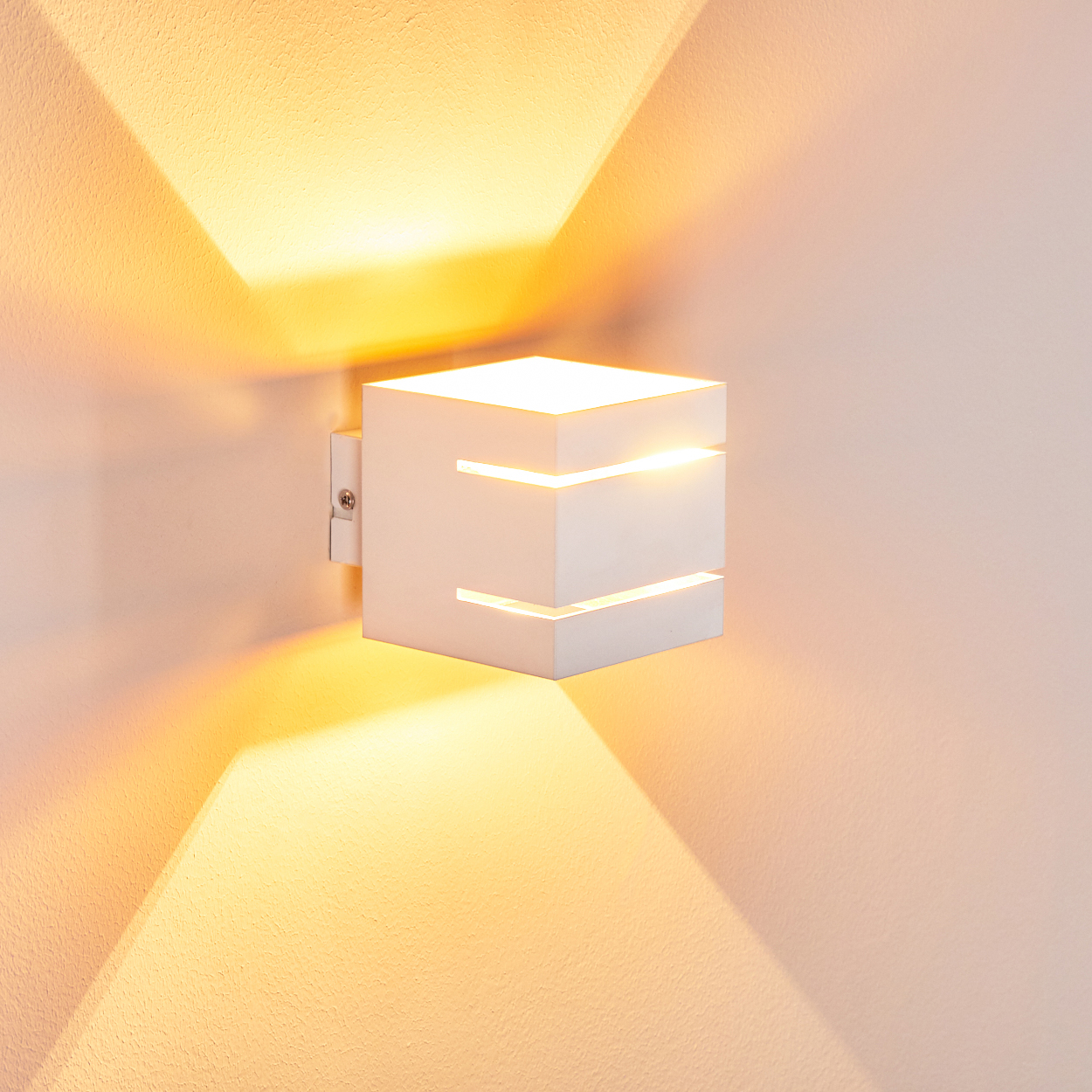 Eine weiße, würfelförmige Wandleuchte ist an einer hellen Wand befestigt. Licht scheint aus der Lampe und wirft dreieckige Schatten.