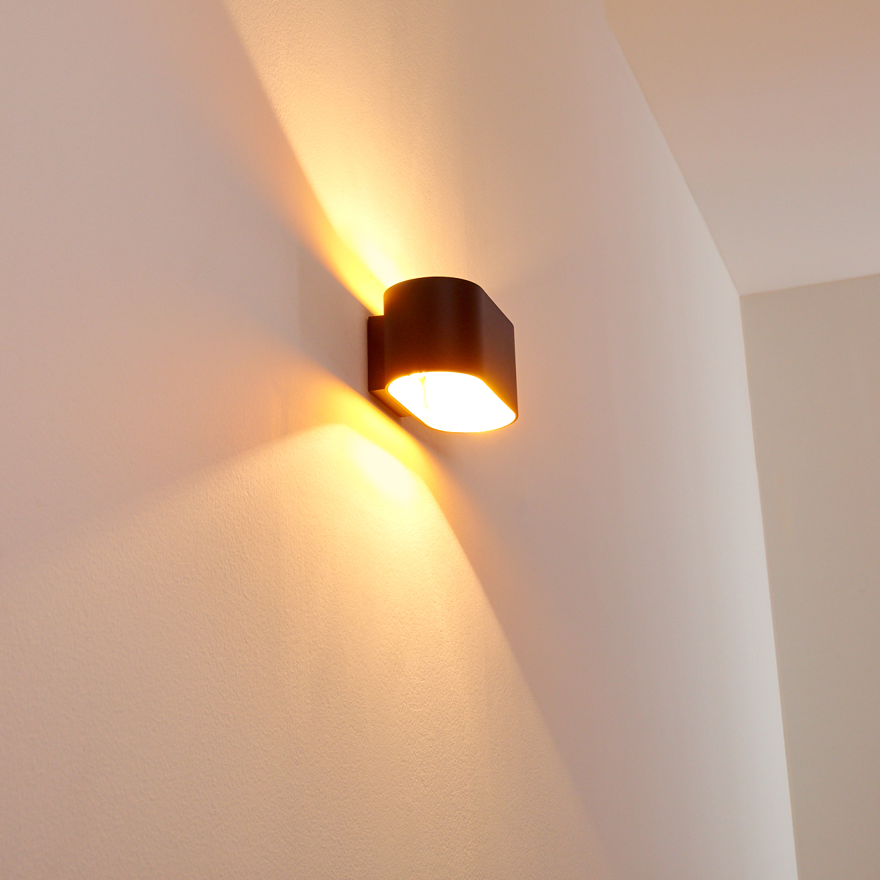 Eine dunkle Wandleuchte strahlt helles Licht auf eine weiße Wand. Die Textur der Wand ist sichtbar, und das Licht wirft Schatten.