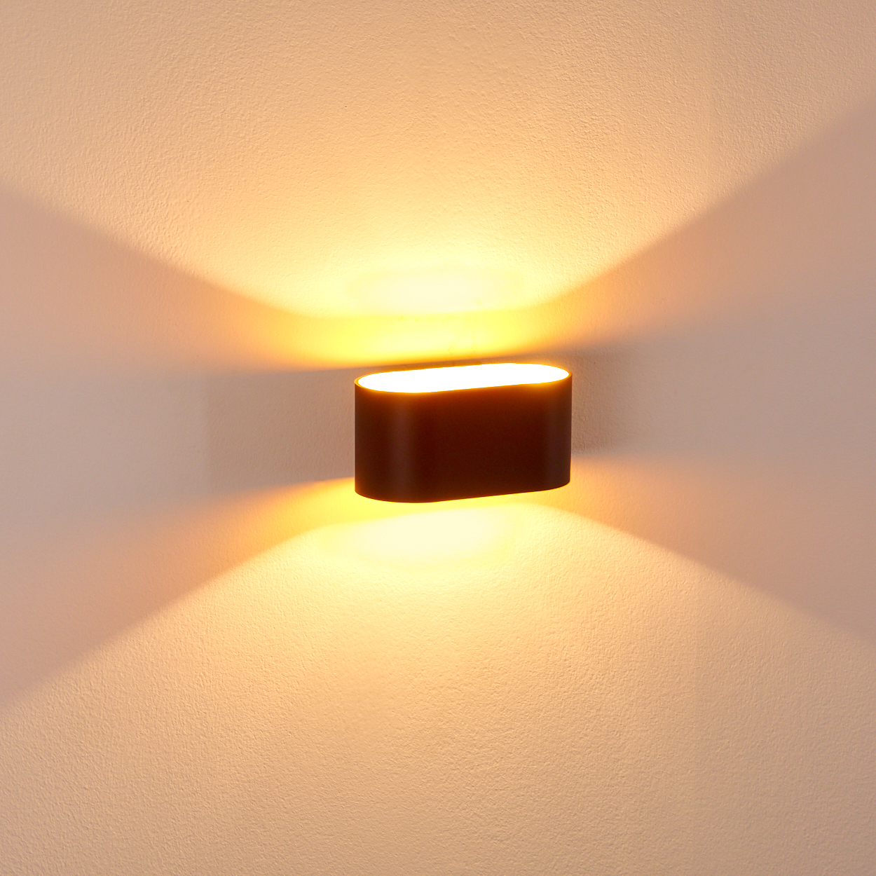 Eine dunkle, ovale Wandleuchte strahlt warmes Licht aus und wirft Schatten auf die strukturierte, beige Wand.