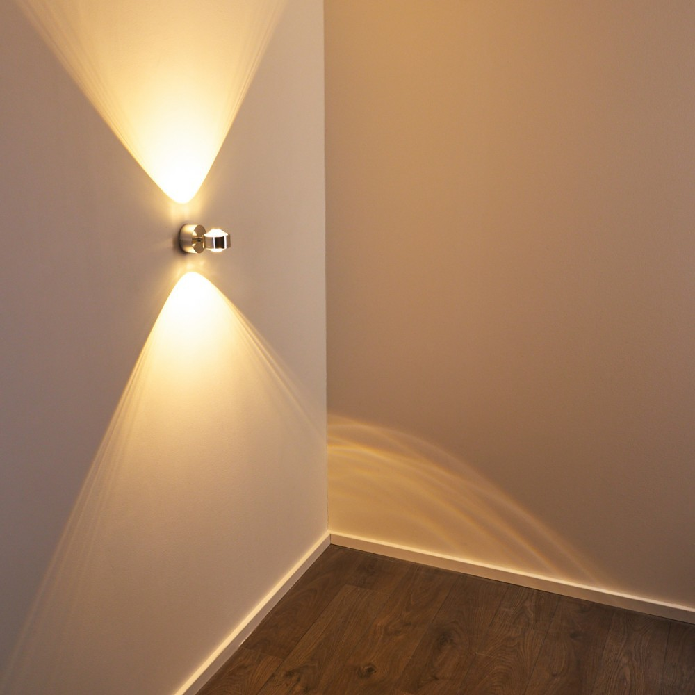 Eine moderne Wandleuchte strahlt nach oben und unten und beleuchtet die Ecke eines Raumes mit Holzboden.