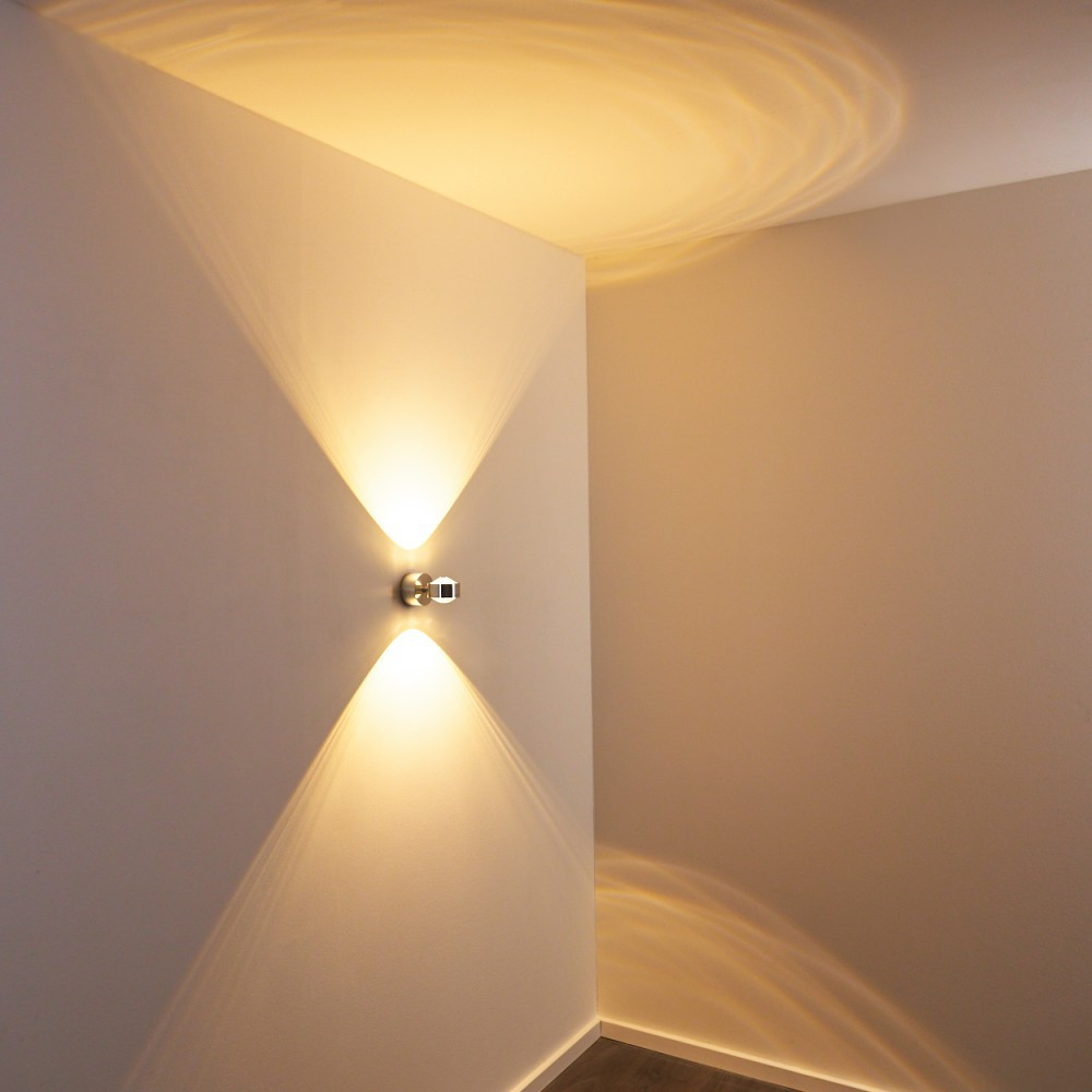 Eine moderne Wandleuchte mit zwei Lichtstrahlen, die die Wand beleuchten. Das Licht erzeugt ein Muster an der Decke und an der Wand.