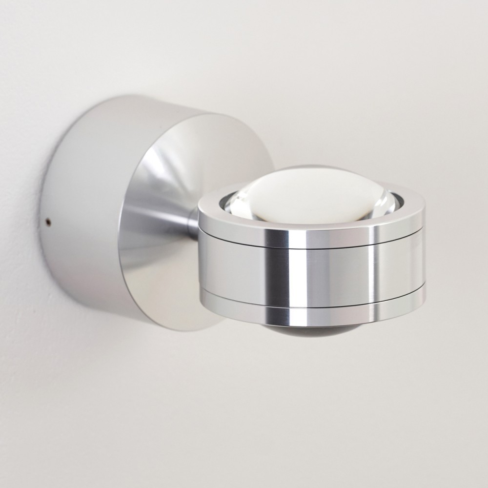 Eine moderne, silberne Wandleuchte mit kreisförmigem Design. Sie hat einen runden Sockel und eine zylindrische Leuchte mit kugelförmiger Glasabdeckung.