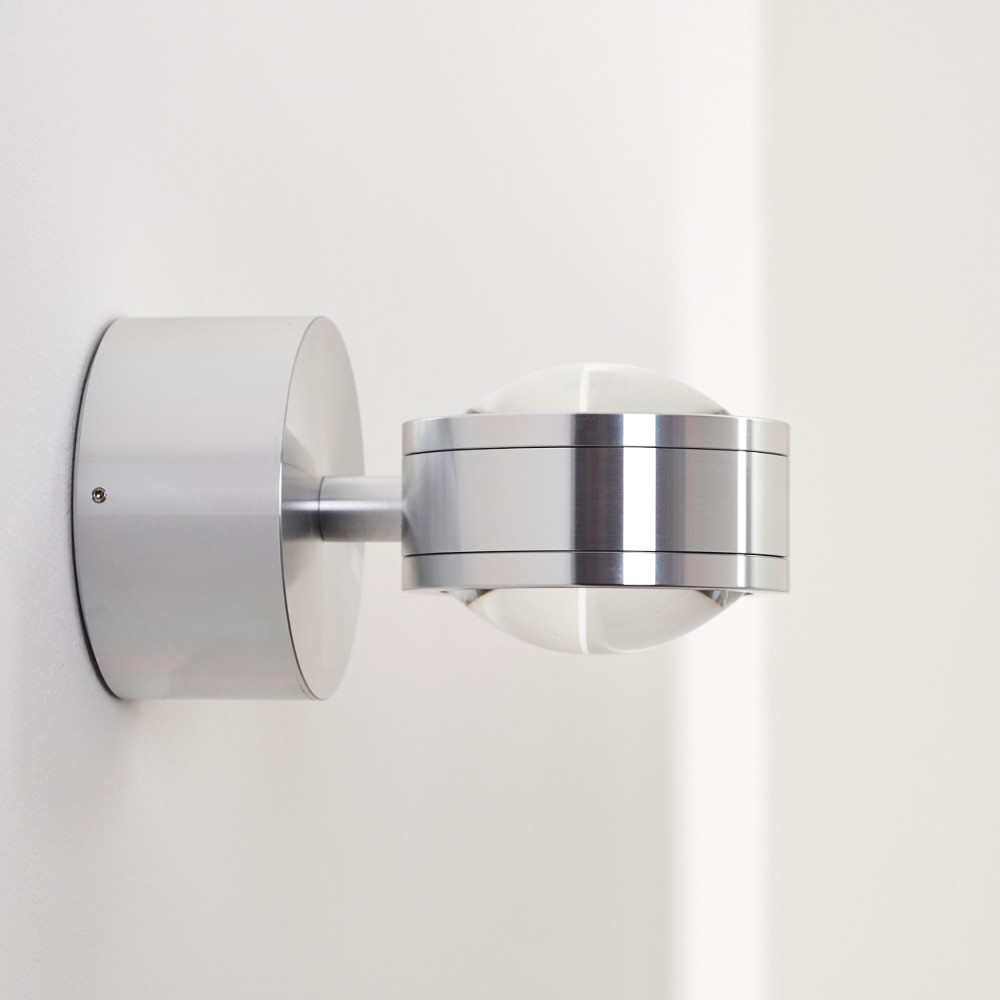 Eine moderne silberne Wandleuchte ist an einer weißen Wand befestigt. Die Lampe hat einen zylindrischen Sockel und einen kugelförmigen Glasschirm.