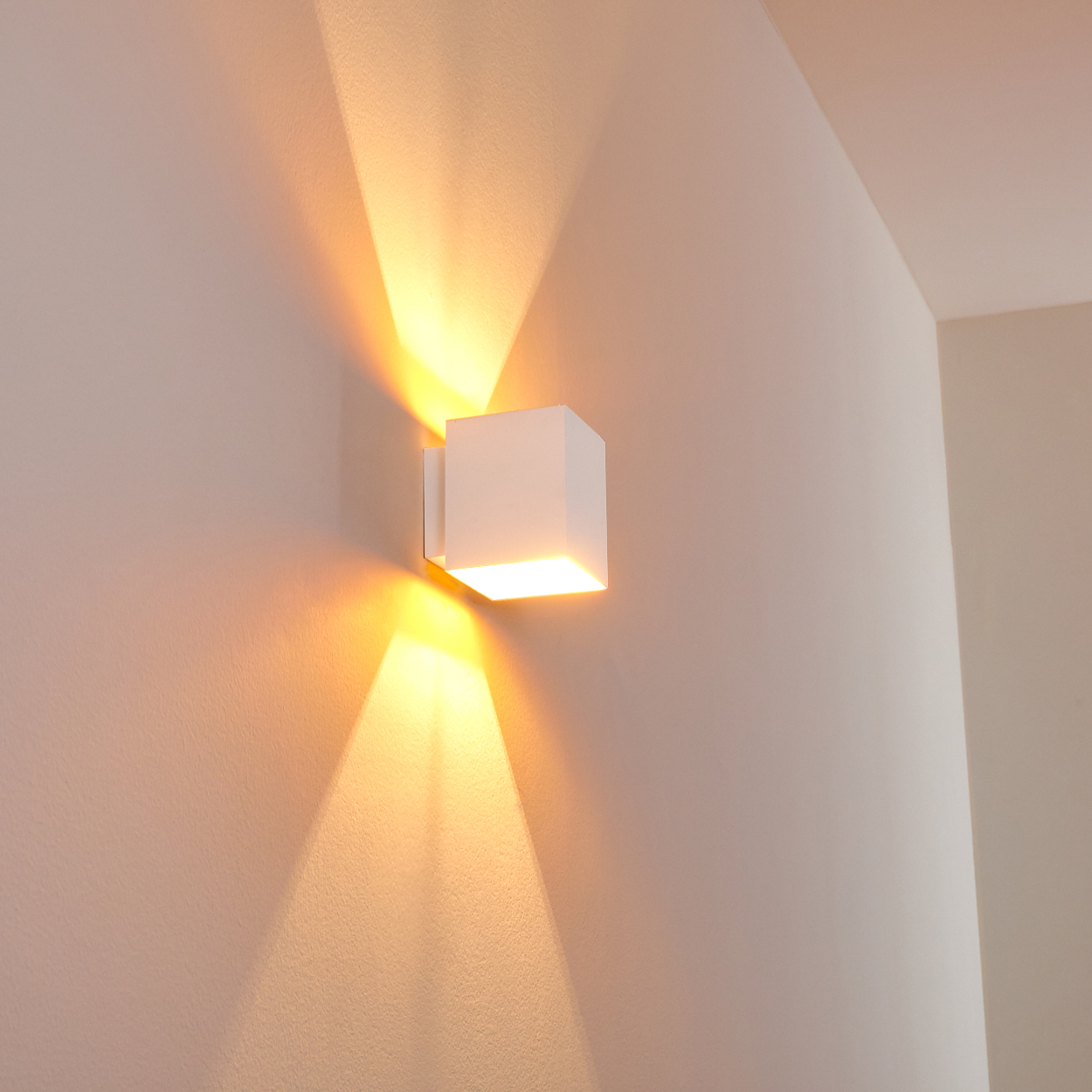 Eine weiße, würfelförmige Wandleuchte beleuchtet die Wand mit warmem Licht und wirft nach oben und unten Schatten.