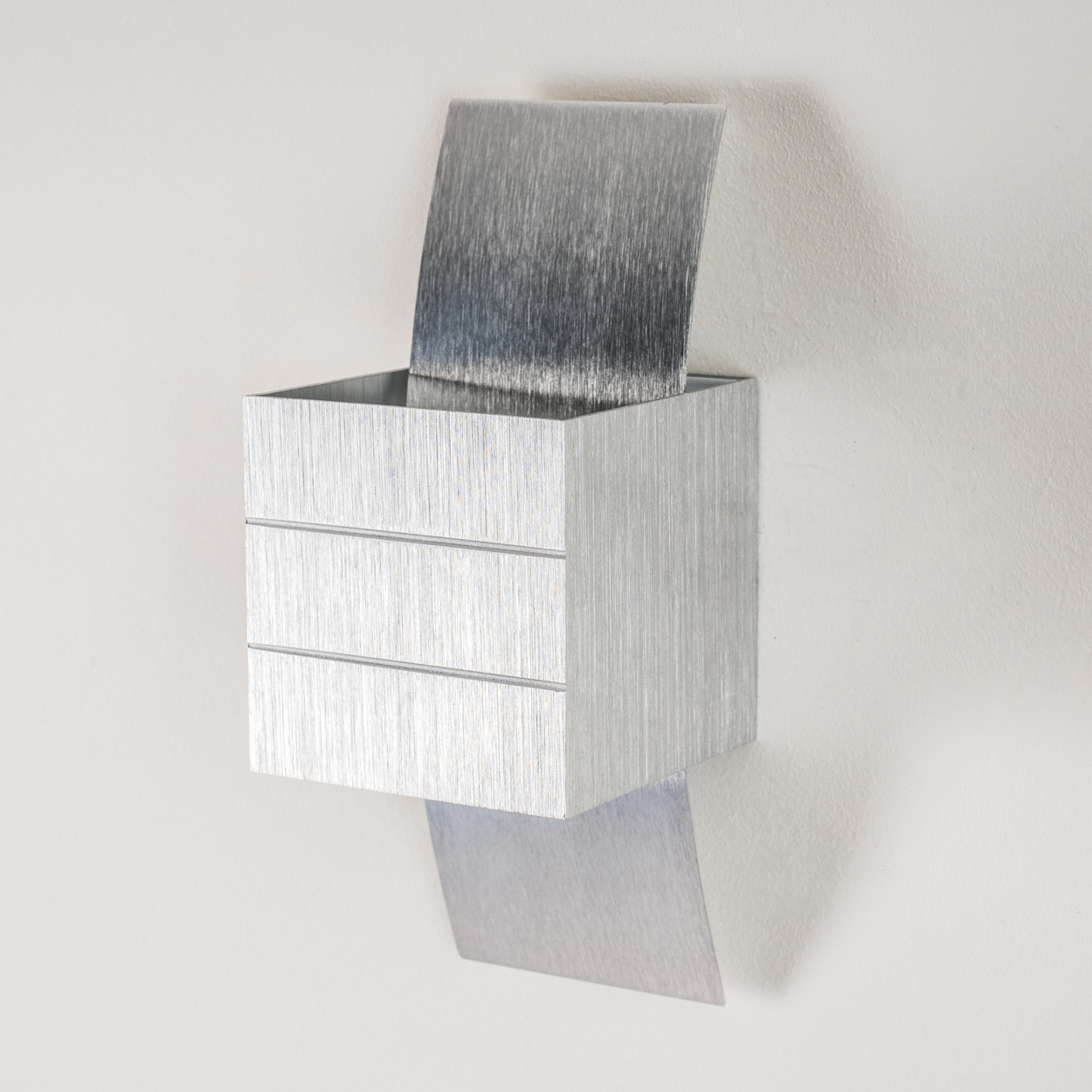 Ein metallischer Kasten mit drei horizontalen Linien und zwei Metallplatten, an einer weißen Wand befestigt. Eine Platte ist oben, die andere unten.